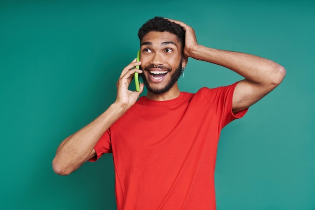 Excited african man talking on mobile phone and smiling while standing against green background