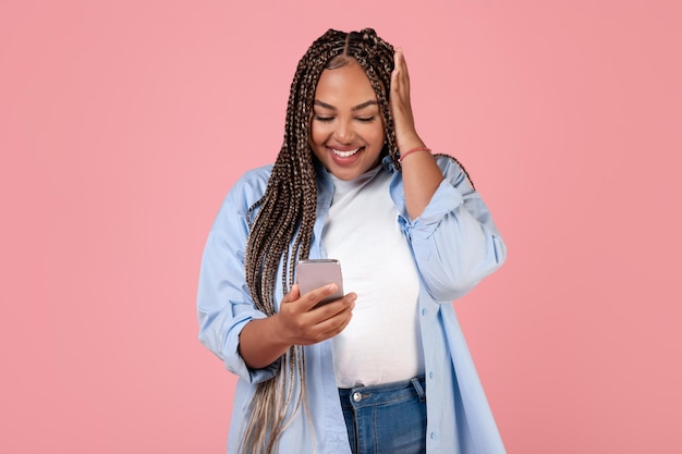 Excited African Woman Using Cellphone Reading Message Texting Pink Background