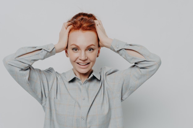 Photo excited amazed redhaired woman holding head in hands and looking at camera with surprised expression