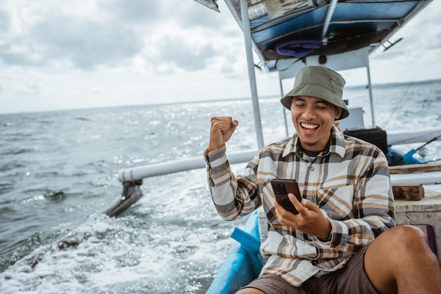 Excited angler using cell phone while sitting resting on fishing boat