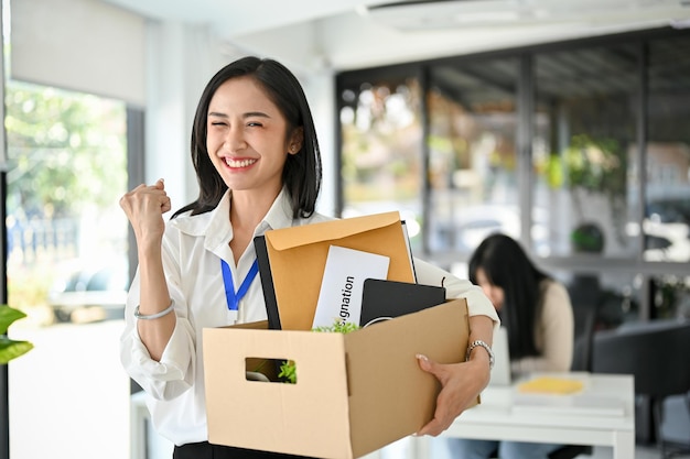 Excited Asian female office worker is celebrating her resignation carrying her personal stuff