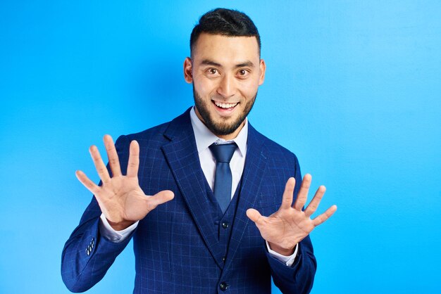 Photo excited asian kazakh man in business suit with tie smiles and throws his hands in surprise, isolated in blue studio