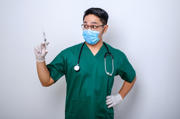 Excited asian male nurse in medical mask rubber gloves and scrubs looking amazed at syringe with vaccine