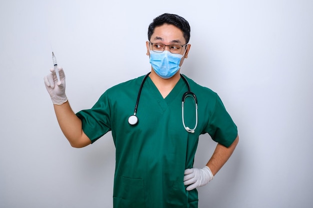 Excited asian male nurse in medical mask rubber gloves and scrubs looking amazed at syringe with vaccine