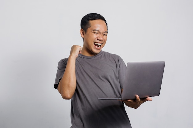 Excited Asian man with winning gesture looking to a laptop