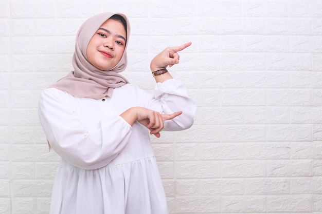 Excited Asian Muslim woman showing advertisement pointing with two hands and fingers to the side