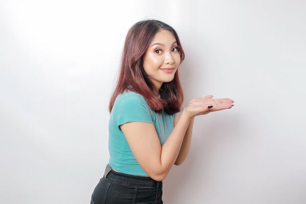 Excited Asian woman wearing blue tshirt pointing at the copy space beside her isolated by white background