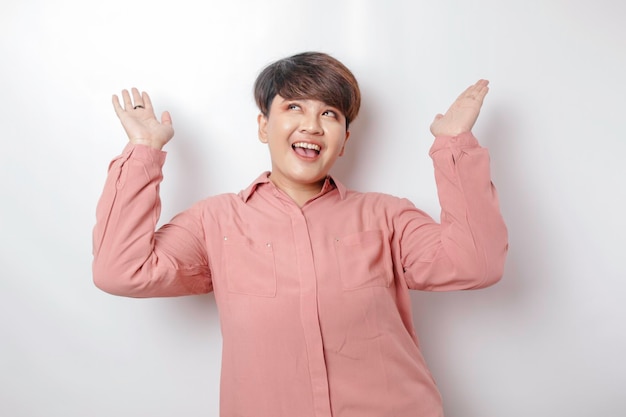 Excited Asian woman wearing pink shirt pointing at the copy space upside her isolated by white background