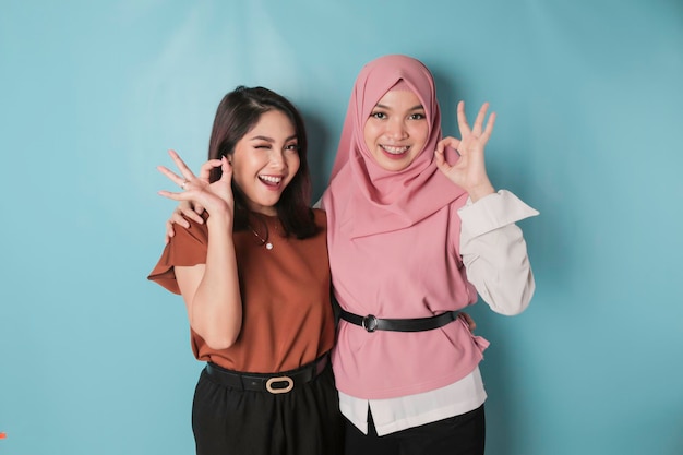 Excited Asian women giving an OK hand gesture isolated by a blue background