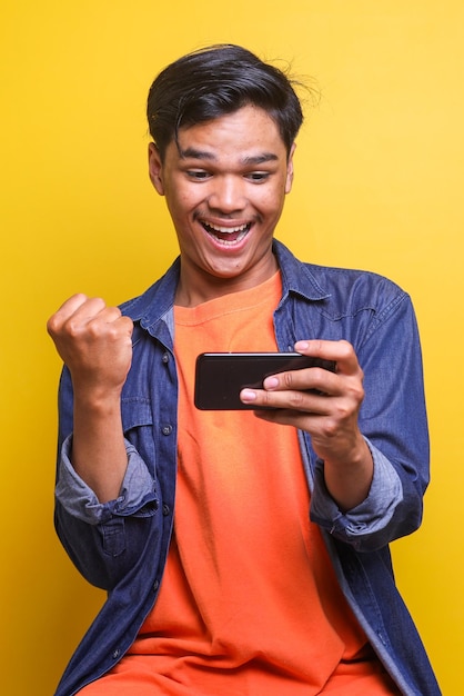 Excited Asian young man looking at mobile phone celebrating victory or winning a game