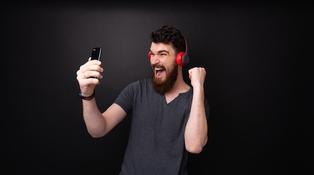 Excited bearded guy,  listening music on headphones, screaming and singing over dark background