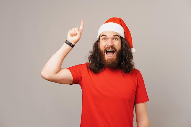 Excited bearded man with long hair points up while wearing a Christmas cap