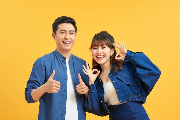 Excited beautiful asian couple shows thumb up gesture agree to do something and collaborate against orange wall, did great job, show approval, like idea. Everything will be OK.