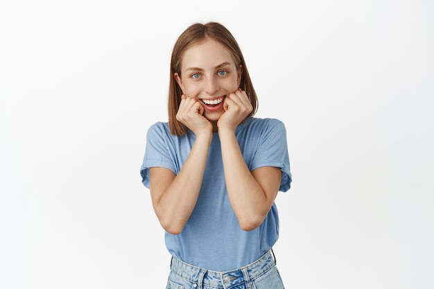 Excited beautiful woman expecting, looks with anticipation and amusement, watching with happy and amazed face, standing thrilled against white wall.