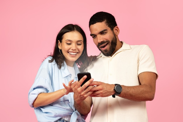 Excited beautiful young couple looking at shining smartphone screen