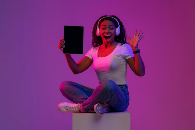 Excited black female holding blank digital tablet in neon light