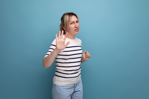 Excited blond girl in a striped sweater on a blue background with copy space