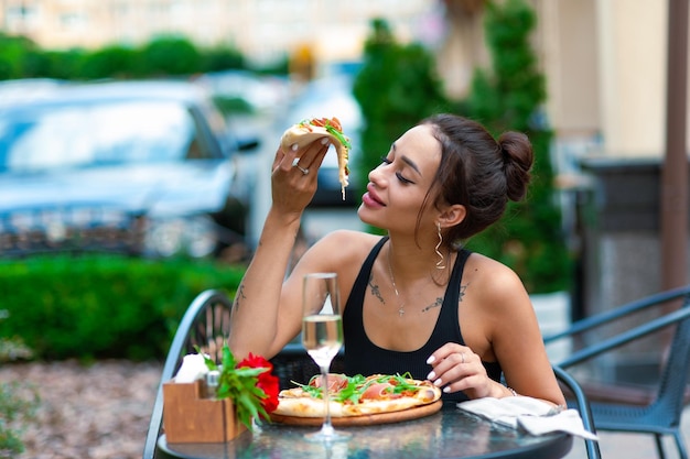 Excited brunette woman with sexy plump lips eats a piece of pizza on the street place for text