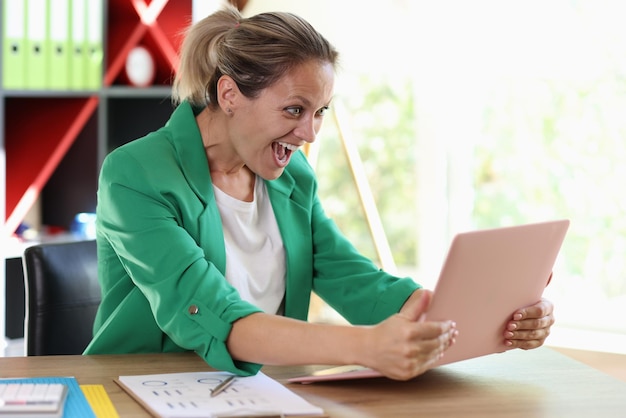 Excited business woman holding her laptop over her work desk and looking at computer screen