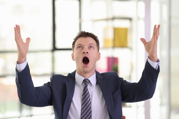 Excited businessman in formal suit screams and raises hands up in company office emotional