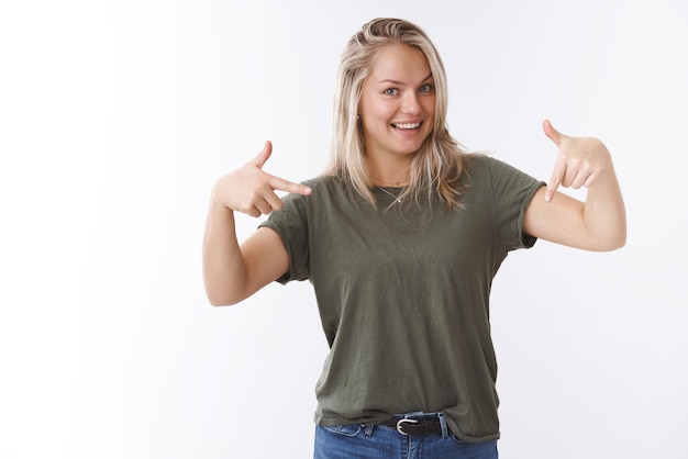 Excited and carefree attractive european blonde asking see down indicating bottom copy space with index finger and smiling mysteriously and cheeky on white