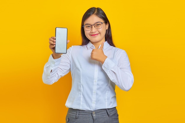 Excited and cheerful asian woman showing blank smartphone screen and thumbs up on yellow background