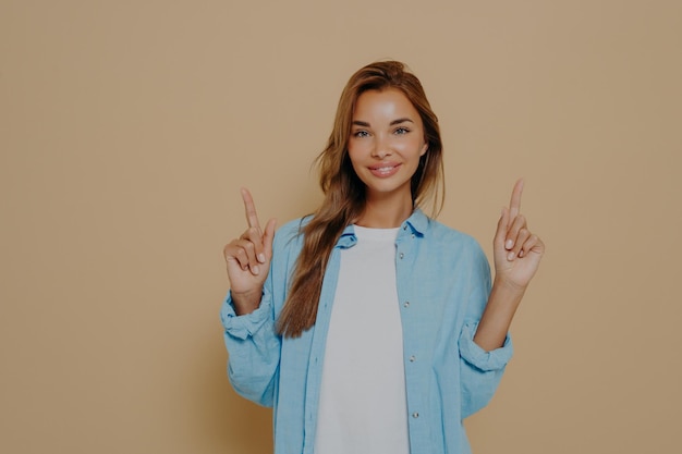 Excited cheerful european female with long brunette hair wearing casual clothes posing in studio