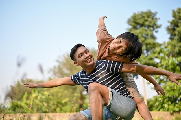 Excited and cheerful young Asian boy piggybacking on his father