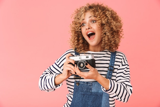 excited curly woman 20s photopraphing on retro camera while standing