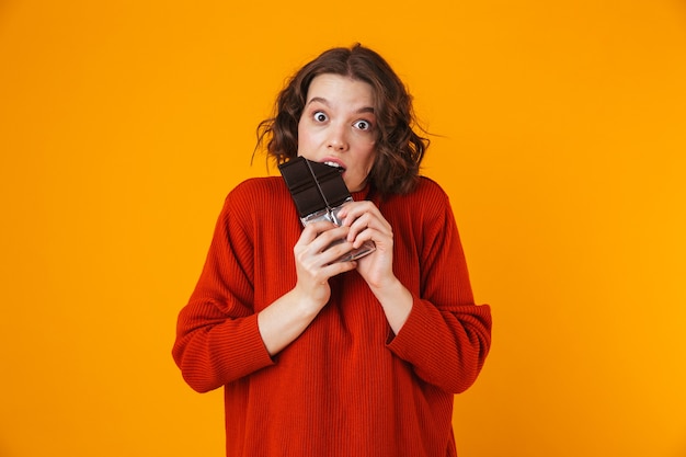 excited emotional young pretty woman posing isolated on yellow wall holding chocolate.