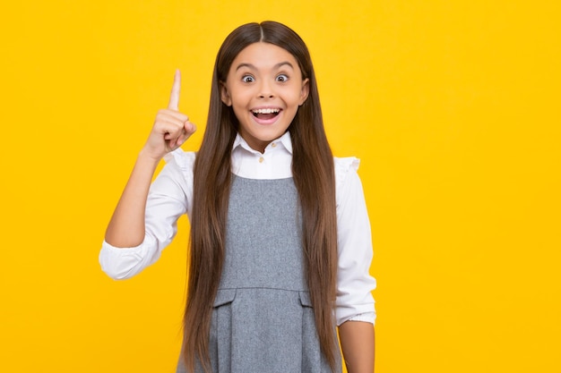 Excited face cheerful emotions of teenager girl Close up funny face of young teenager pointing up with finger on yellow background Girl has great new idea Funny schoolgirl kid genius nerd