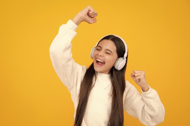 Excited face Teen girl in headphones listen to music Wireless headset device accessory Child enjoys the music in earphones on yellow background Amazed expression cheerful and glad