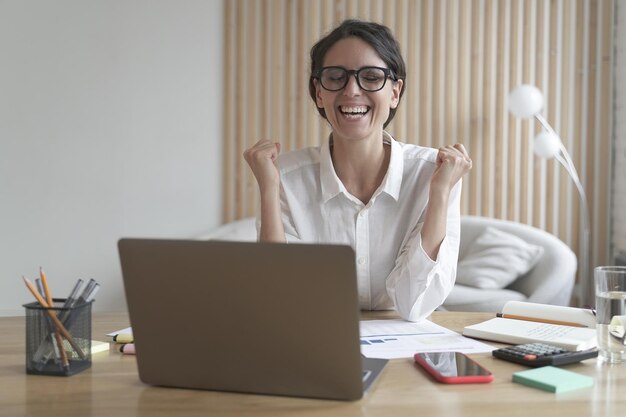 Excited female employee in glasses celebrating success achievement or good work results