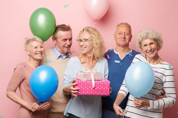 Excited friends congratulating mature lady with birthday