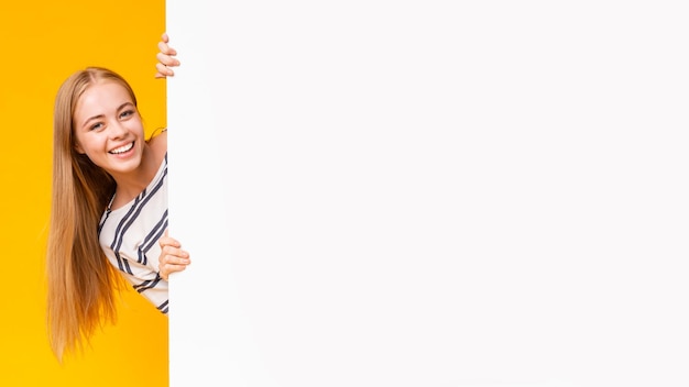 Photo excited girl looking from behind blank advertising board