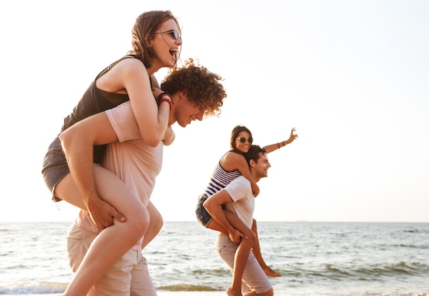 Excited group of friends loving couples walking outdoors on the beach having fun