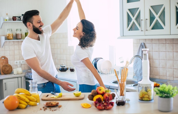 Excited happy beautiful young couple in love cooking in the kitchen and having fun together while dancing and smiling