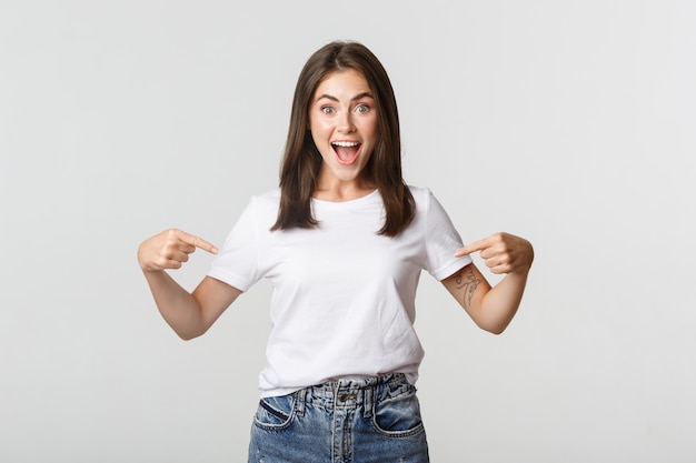 Excited happy brunette girl smiling, pointing fingers at logo