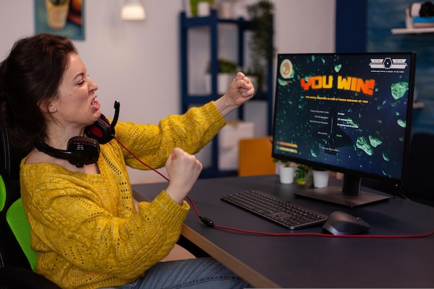 Excited happy competitive winner woman gamer winning space shooter videogames during online championship celebrating game at home in living room. Player playing on RGB powerful computer