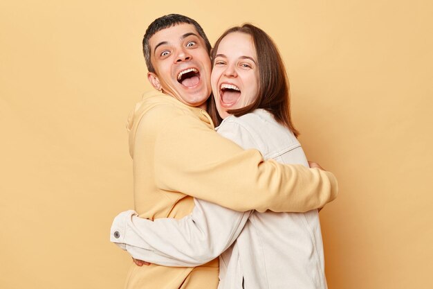 Excited happy friends woman and man wearing casual style clothing standing isolated over beige background hugging each other and laughing happily