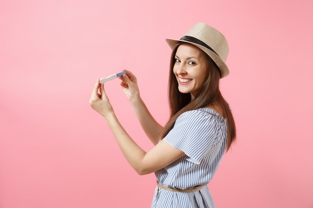 Excited happy woman in blue dress, hat hold in hand, looking at pregnancy test isolated on pink background. Medical healthcare gynecological, pregnancy fertility maternity people concept. Copy space.