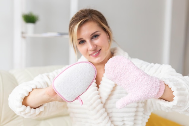 Excited joyful young woman wrapped head in towel holding dry brush shower sponge and doing spa procedure