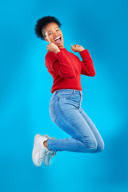 Excited jump and woman portrait with winner deal and smile in a studio Wow energy and up in the air with female person and blue background with celebration for sale announcement and big news