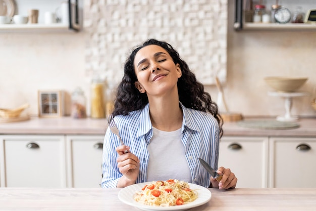 Excited lady enjoying delicious homemade pasta eating tasty lunch with closed eyes while sitting at