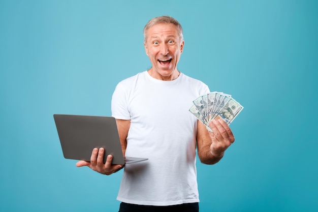 Excited mature man holding money cash and pc