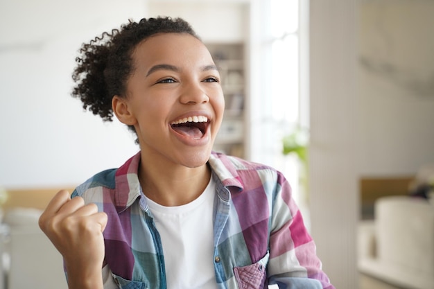 Excited mixed race teen girl makes yes winner hand gesture celebrates success personal achievement