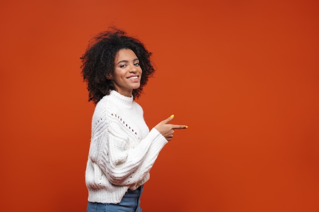 Excited pretty young african woman standing isolated over red wall, presenting copy space