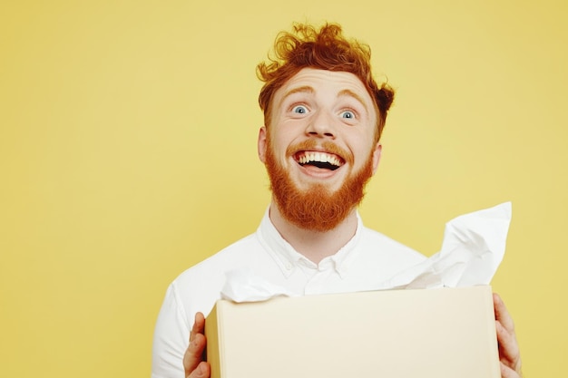 Photo excited redhead man unboxing surprise gift against yellow background