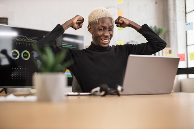 Excited screaming young african business man or entrepreneur working with laptop computer