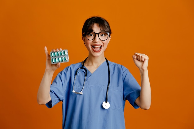 excited showing yes gesture holding pills young female doctor wearing uniform fith stethoscope isolated on orange background